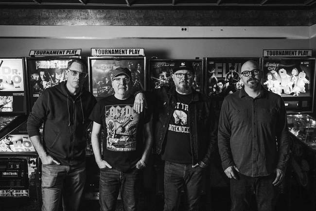 A portrait of the Smoking Popes standing in front of pinball machines