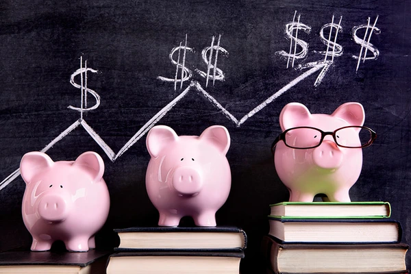 Three pink piggy banks standing on books next to a blackboard with simple savings progress chart.