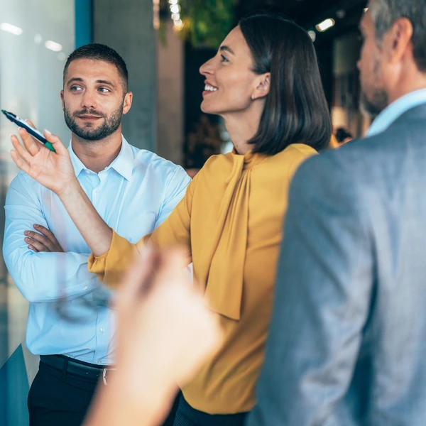 coworkers in a startup brainstorming strategies, writing a business plan on whiteboard to his team on a meeting