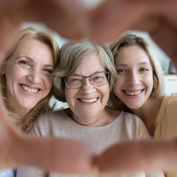 Joyful happy loving grandma, mature mother and young adult granddaughter woman looking, smiling at camera through hand heart frame. Cute portrait of loving three family female generations having fun
